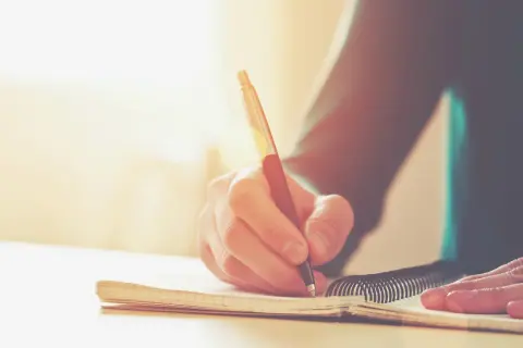 Main d'une personne écrivant dans un carnet. Une histoire vraie prend forme, un témoignage précieux consigné dans ce livre.
