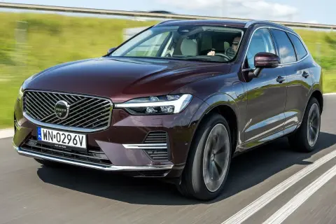Elegancki, bordowy Volvo XC60 T5 w ruchu drogowym. Kierowca w okularach prowadzi SUV-a po asfaltowej drodze, otoczonej zielenią.