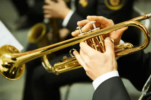 Hände spielen eine glänzende Trompete. Ein Musiker bereitet sich auf sein Referat vor, während im Hintergrund ein Saxophon zu sehen ist.