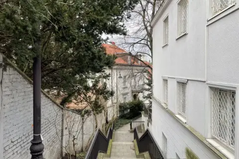 Schody prowadzące do starego domu, gdzie trwa wymiana okien. Widać biały budynek z kratami i drzewa.