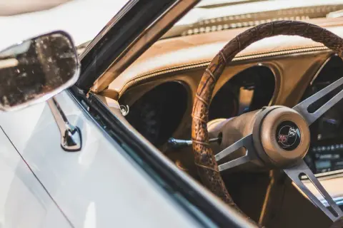 Detaljer från en klassisk bil. Ratt, instrumentbräda och dörrsida i brunt läder. Perfekt för att lära sig hur startar man en manuell bil.