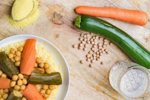 Un plat de couscous aux légumes, pois chiches, carottes et courgettes. Une cuillère de semoule est à côté.