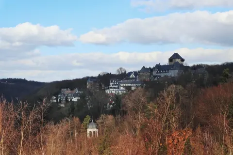 Blick auf Schloss Burg, das majestätisch auf einem Hügel thront, umgeben von Bäumen. Ein kleiner Pavillon im Vordergrund, im winterlichen Wupper Tal.