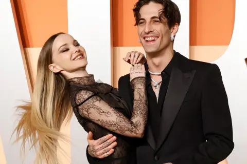 La pareja Dove Cameron y Dylan Sprouse ríen juntos, ella con un vestido de encaje negro y él con un traje negro.