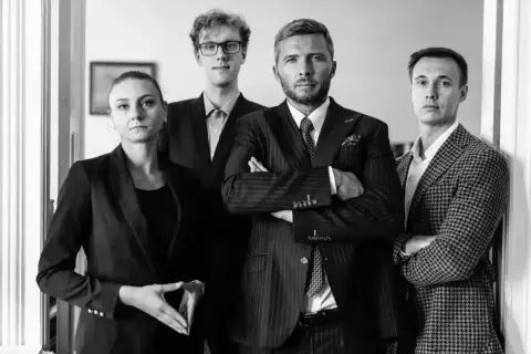 Cztery osoby w garniturach, dwie kobiety i dwóch mężczyzn, stoją w rzędzie.