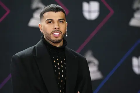 Rauw Alejandro, de Puerto Rico, posa con un traje negro y un suéter de red.