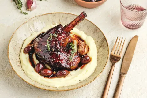 Une souris d'agneau braisée, nappée d'une sauce foncée, servie sur une purée onctueuse avec des olives et de l'ail rôti.
