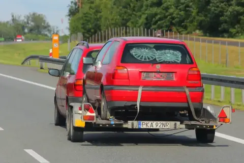 Czerwony Volkswagen Golf na lawecie, holowany przez inny samochód. To dowód, że automatem można holować inne auto, choć nie jest to standardowa sytuacja.