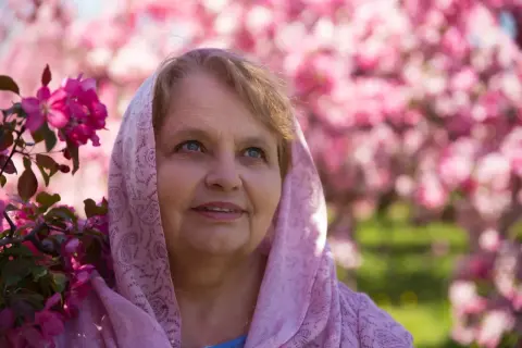 Uśmiechnięta Zuzanna w różowym szalu, otoczona kwitnącymi drzewami. Piękny dzień na imieniny Zuzanny.