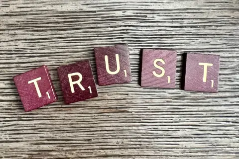 Litery "TRUST" ułożone na drewnianym tle. Brak zaufania w związku czy to ma sens?