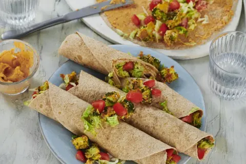 Leckere wraps vegetarisch gefüllt mit geröstetem Brokkoli, Tomaten und Salat. Dazu ein Dip und ein Glas Wasser.