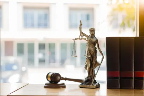 Figurka Temidy, symbol sprawiedliwości, obok młotka sędziowskiego i ksiąg. To alegoria co to znaczy dla prawa.