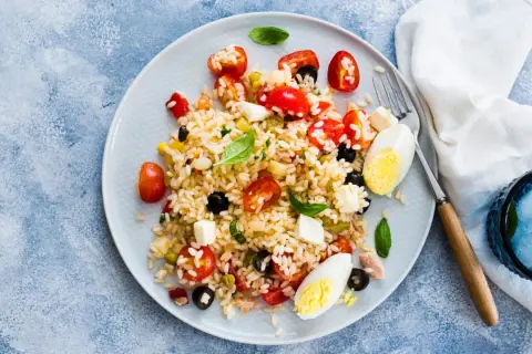 Un piatto colorato di insalata di riso con pomodorini, olive, mozzarella e uova sode. Perfetta per un pasto estivo.
