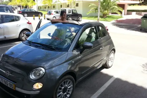 Frau lehnt sich aus einem grauen Fiat 500 Cabrio, bereit für eine Spritztour. Gute mietwagen portugal tipps für den Urlaub!