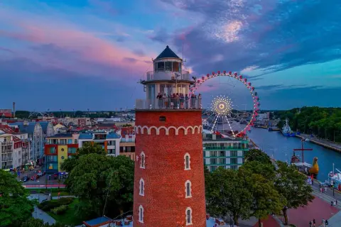 Widok na latarnię morską, diabelski młyn i port w Kołobrzegu o zachodzie słońca.