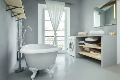 Un baño moderno con bañera independiente, lavadora y estantes con toallas. La idea de pintar bañera aquí es para un estilo minimalista.