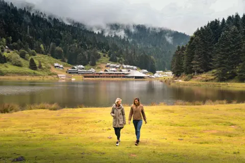 Deux amies profitent d'une promenade au bord du lac de Payolle, entouré de forêts et de montagnes brumeuses.
