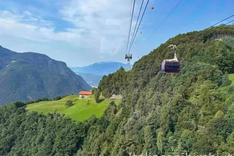 Cabina del trenino del Renon in viaggio tra boschi e montagne, con una casa su un prato verde. Cosa vedere in questo paesaggio mozzafiato.