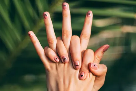 Manos con uñas flamencas en tono rosa pálido, decoradas con pequeños triángulos y puntos negros.