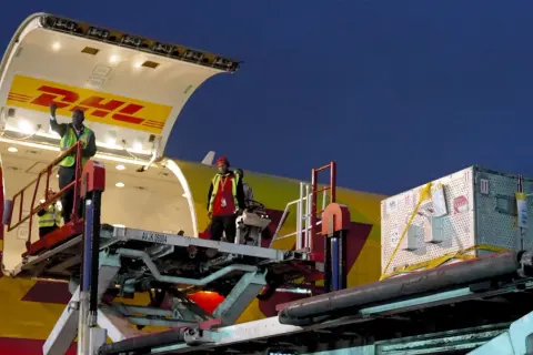 Pracownicy rozładowują samolot DHL. Z jakiego kraju pochodzi ten transport?