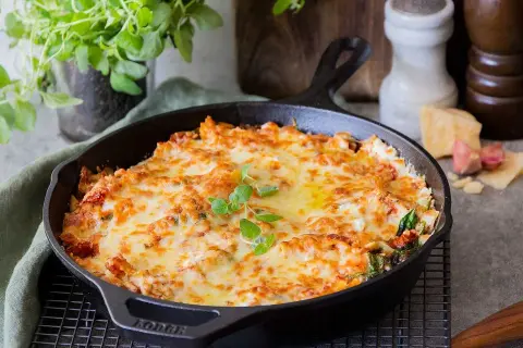 En gyllene, bubblande vegetarisk lasagne i gjutjärnspanna, toppad med färska örter. Perfekt för en mysig middag.