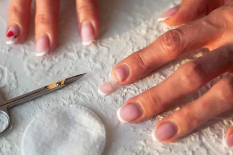 Dłonie z francuskim manicure, nożyczki i wacik. Zastanawiasz się, dlaczego nie rosną paznokcie u rąk? Może to kwestia pielęgnacji.