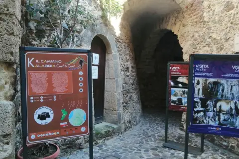 Cartello informativo sul Cammino Calabria Coast to Coast, con scorci di antiche costruzioni in pietra.