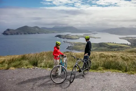 Pareja disfrutando de un paseo en bicicleta por la costa de Irlanda, con vistas a islas y montañas.