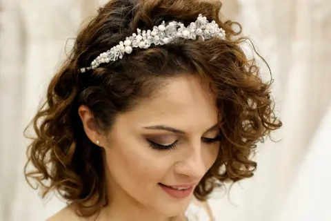 Brautfrisur kurze Haare Bob mit funkelndem Diadem. Lockige Haare umrahmen das Gesicht einer lächelnden Braut.