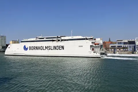 Biały prom "Bornholmslinjen Express" wypływa z portu, gotowy na podróż do Szwecji. W tle widać zabudowania portowe.
