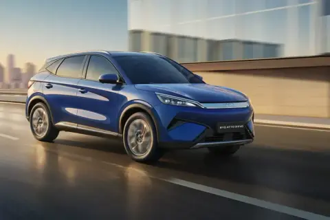 Niebieski BYD ATTO 3 EVO pędzi po drodze, z miastem w tle.