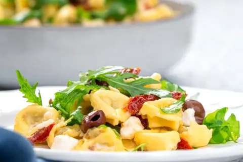 Ein köstlicher italienischer Salat mit Tortellini, Rucola, Oliven und getrockneten Tomaten auf einem Teller.
