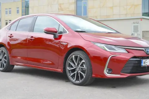 Czerwona Toyota Corolla 1.8 Hybrid z nowoczesnymi felgami stoi przed budynkiem.