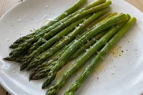 När man ska koka sparris är det viktigt att den blir perfekt. Här ligger en vackert grön, nykokt sparris på ett fat, strödd med flingsalt och peppar.