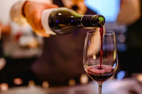 Ciemnoczerwone bordeaux wino leje się z butelki do kieliszka, tworząc piankę.