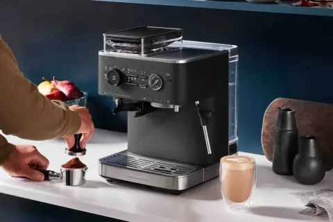 Un uomo prepara il miglior caffè con una macchina KitchenAid. Un bicchiere di cappuccino fumante attende sul bancone.