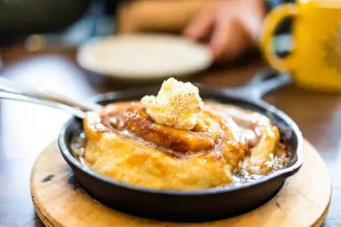 Ein warmer Zimtschnecken-Auflauf in einer Gusseisenpfanne, gekrönt mit Butter. Perfekt, um den Zimtgeschmack zu neutralisieren und den Genuss zu steigern.