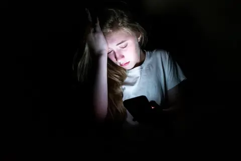 En tonåring med handen mot pannan, upplyst av en mobilskärm. Känslan av depression hos barn kan testas genom att observera sådana här stunder.