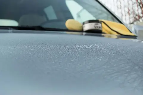 Krople wody na masce samochodu po woskowaniu. W tle widać gąbkę i słoik z woskiem.