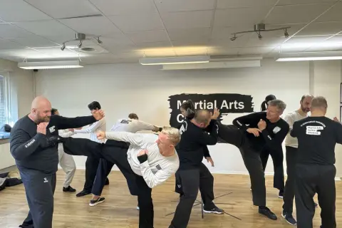 Män tränar wing chun i en lokal. En man utför en hög spark medan andra övar försvar.