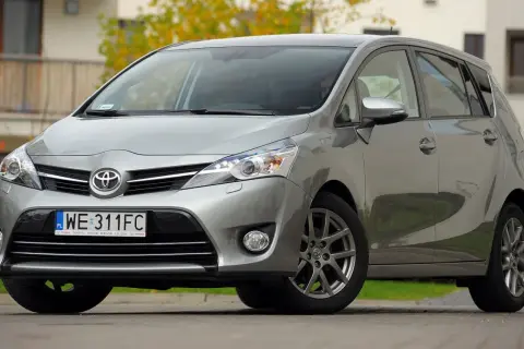 Srebrna Toyota Verso 1.8 benzyna zaparkowana przed budynkiem.