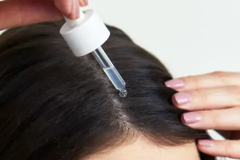 Eine Pipette mit Serum tropft auf die Kopfhaut, um das Haarwachstum mit Retinol zu fördern.