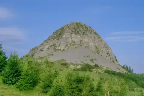 Le rocher de Sampzon, imposant et rocheux, se dresse sous un ciel bleu. Des arbres verts l'entourent.