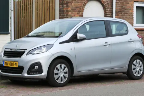 Srebrny Peugeot 108 stoi zaparkowany na brukowanym podjeździe, obok ceglanego domu.