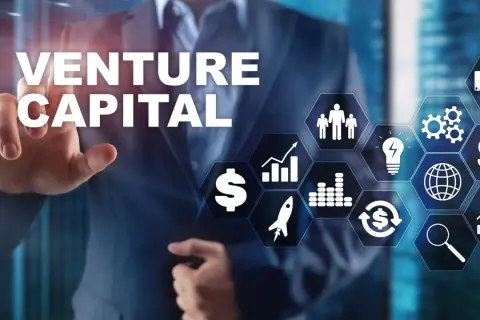 Biznesmen wskazuje na ekran z napisem VENTURE CAPITAL i ikonami symbolizującymi rozwój, pieniądze i innowacje.