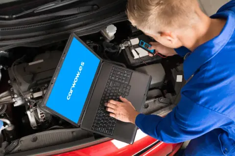 Mecánico revisa el motor de un coche con un portátil y un dispositivo de diagnóstico. El **stage** de la revisión es crucial para el **significado** del buen funcionamiento.