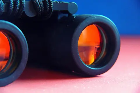 Primo piano di un binocolo nero con lenti arancioni, pronto per esplorare il mondo.