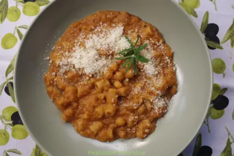 Pyszny makaron z ciecierzycy w sosie pomidorowym, posypany parmezanem i gałązką rozmarynu.