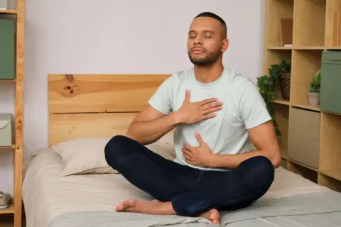 Man meditating on bed, practicing a breathing exercise to fall asleep in 60 seconds.