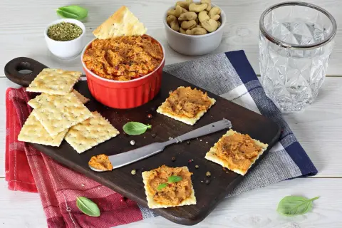 Pasta z suszonych pomidorów na krakersach, podana na desce z dodatkami.